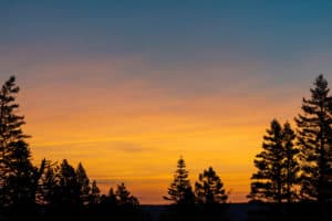 Sunrise from the hilltops overlooking Idaho framed by dark unlit trees.