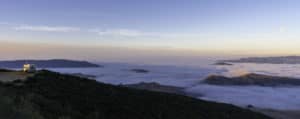 Clouds fill the valley below with a dense layer of fog as the moon sets to the west and the sun rises in the east.